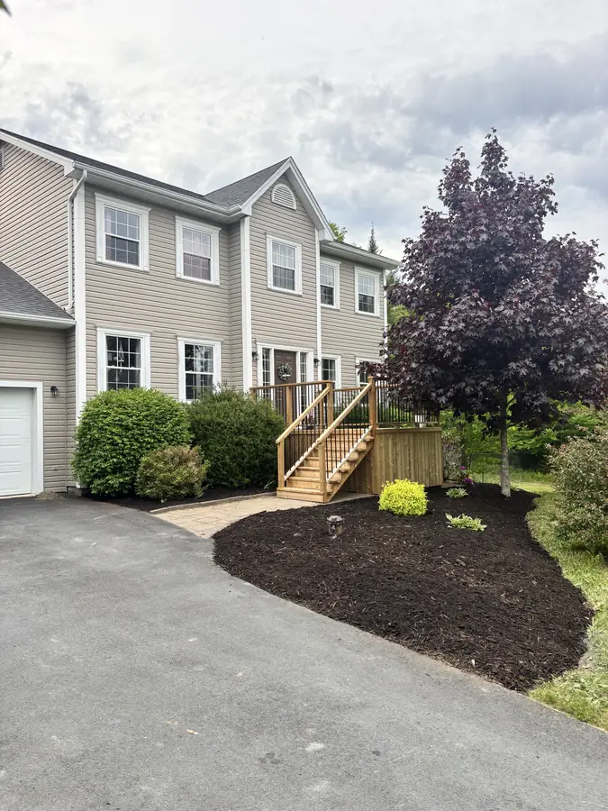 Colonial-style home with a curved black mulch bed, shrubs and a purple-leaf tree along the driveway — landscaping project in Halifax, Nova Scotia