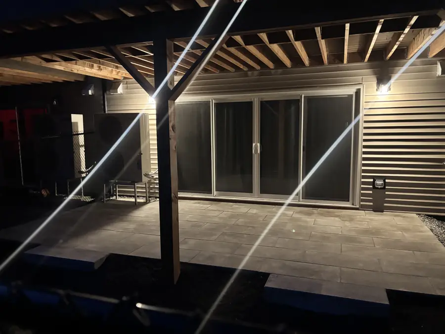 Stone patio and covered deck lit at night in front of sliding glass doors — hardscaping project in Halifax, Nova Scotia