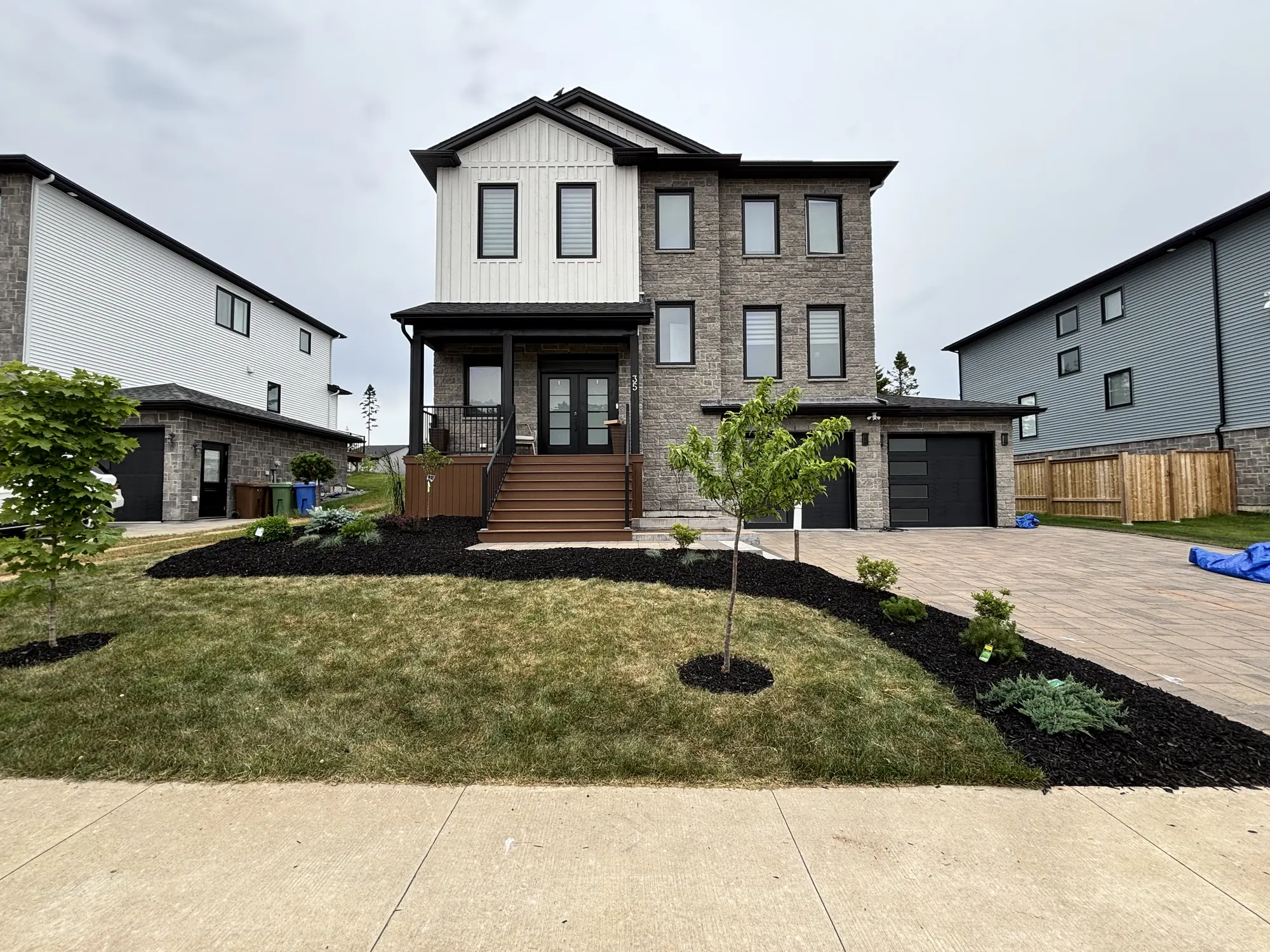 Modern two-storey home with a freshly landscaped front yard, black mulch beds, a young tree and a paver driveway