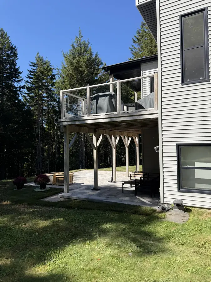 Stone patio and seating area beneath an elevated deck at a modern two-storey home — hardscaping project in Halifax, Nova Scotia