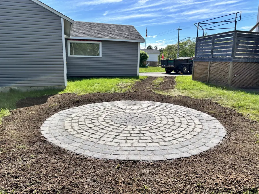 Round paver feature laid in a freshly graded backyard with a deck and fence behind — hardscaping project in Halifax, Nova Scotia